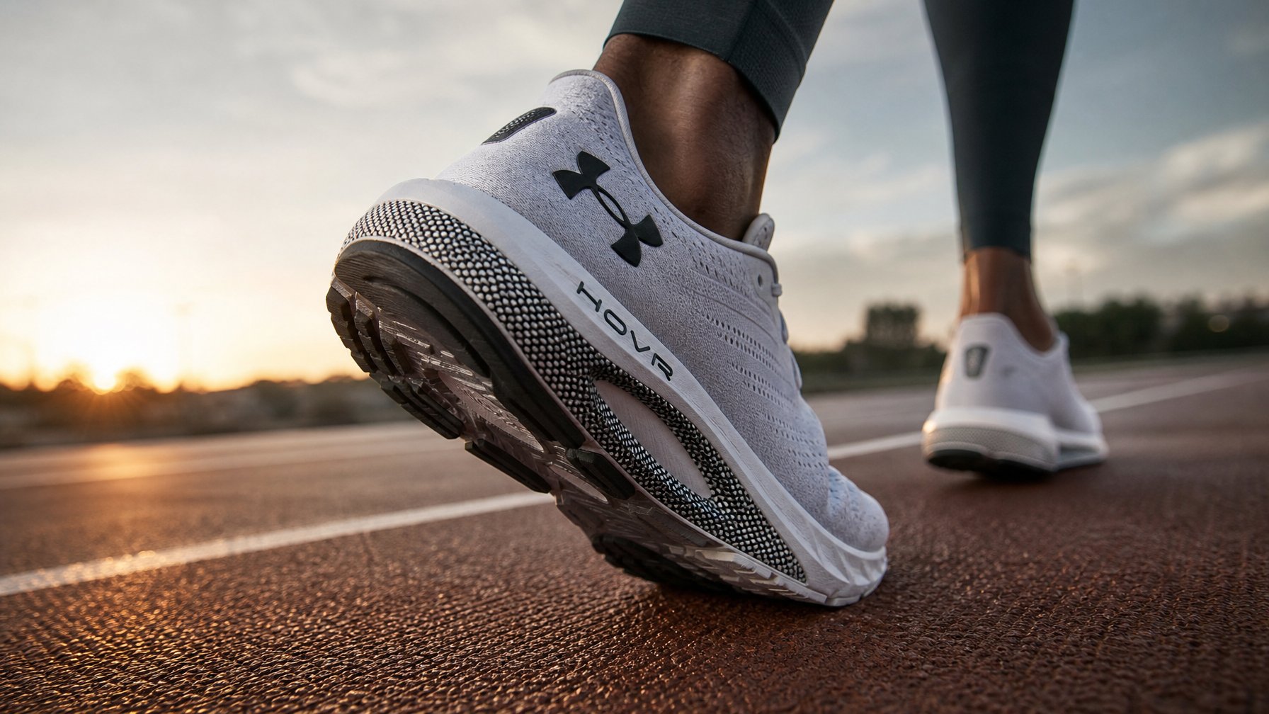 Seorang pelari sedang berlari di trek luar ruangan memakai sepatu lari Under Armour HOVR dengan fokus pada sepatu dan gerakan kaki.