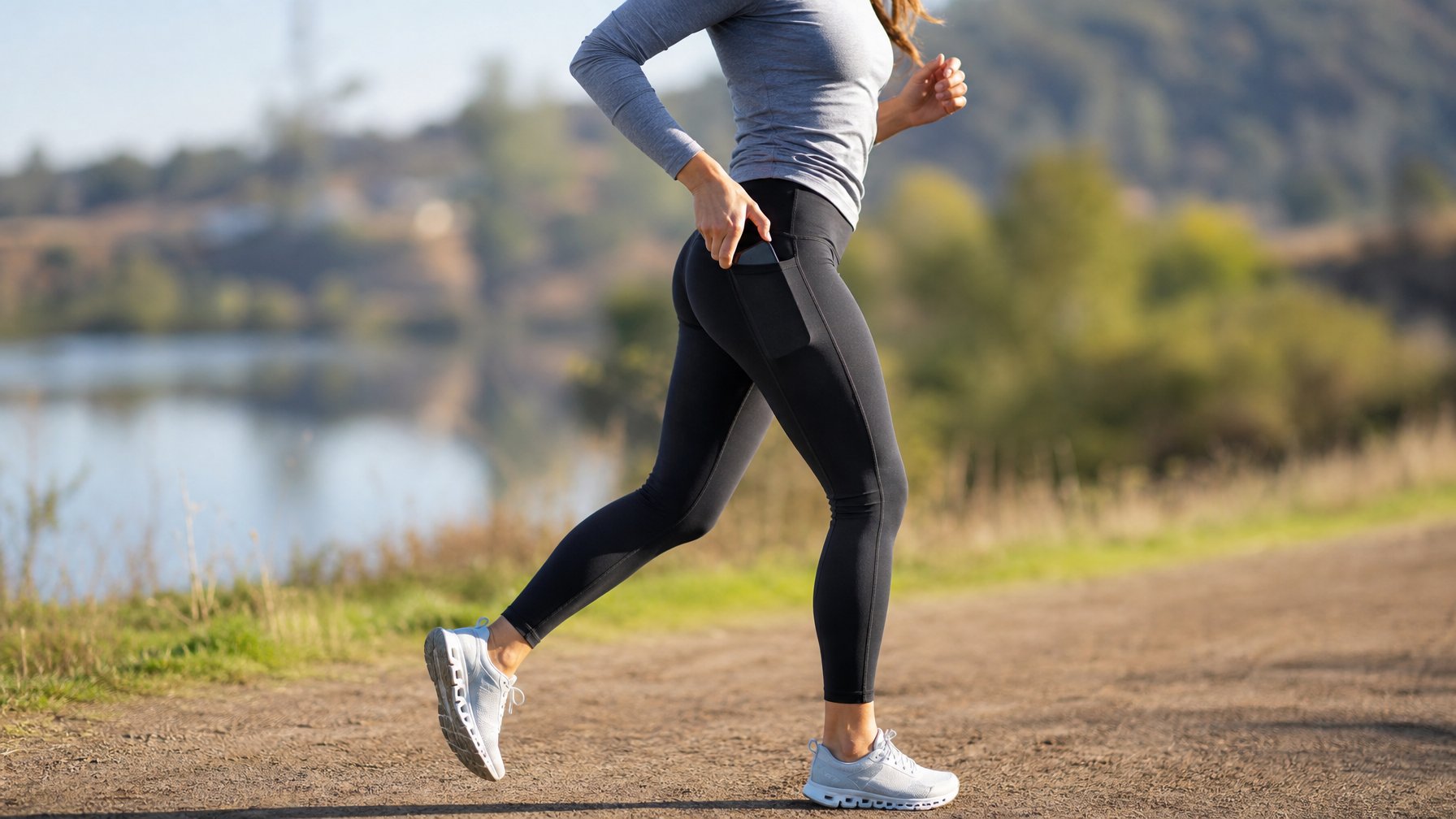 Seorang wanita berlari di jalur outdoor mengenakan celana legging olahraga dengan saku di samping.