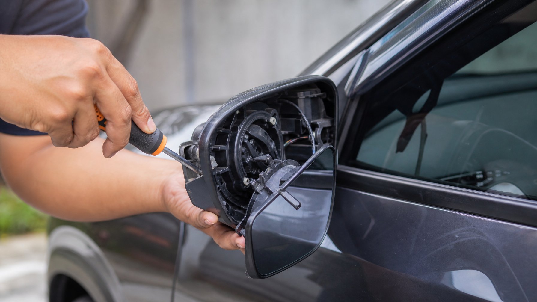 Tangan seseorang sedang memperbaiki spion mobil yang patah di luar ruangan.