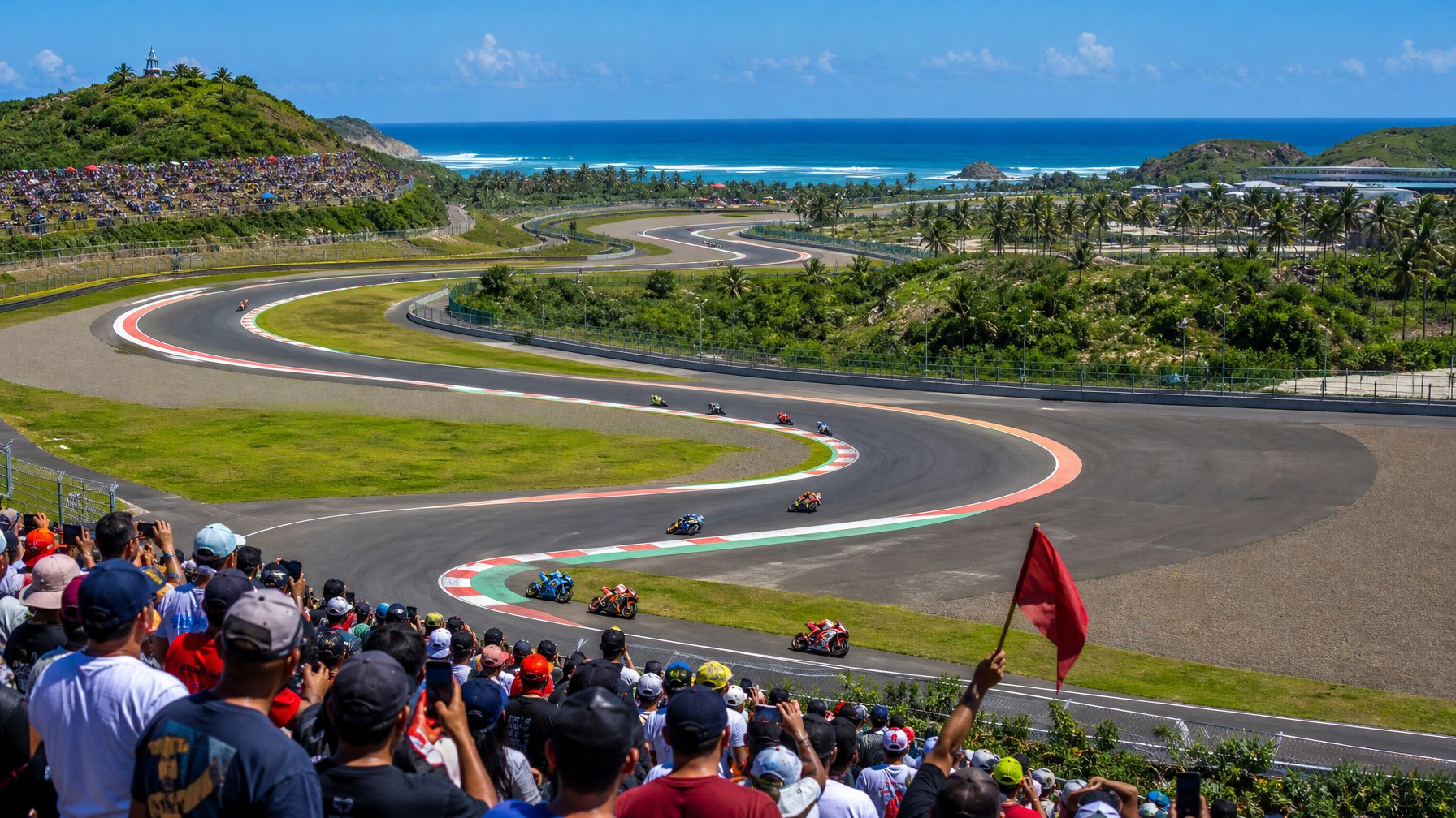 Pemandangan sirkuit Mandalika dengan motor MotoGP melaju di lintasan dan penonton di tribun yang menikmati balapan.