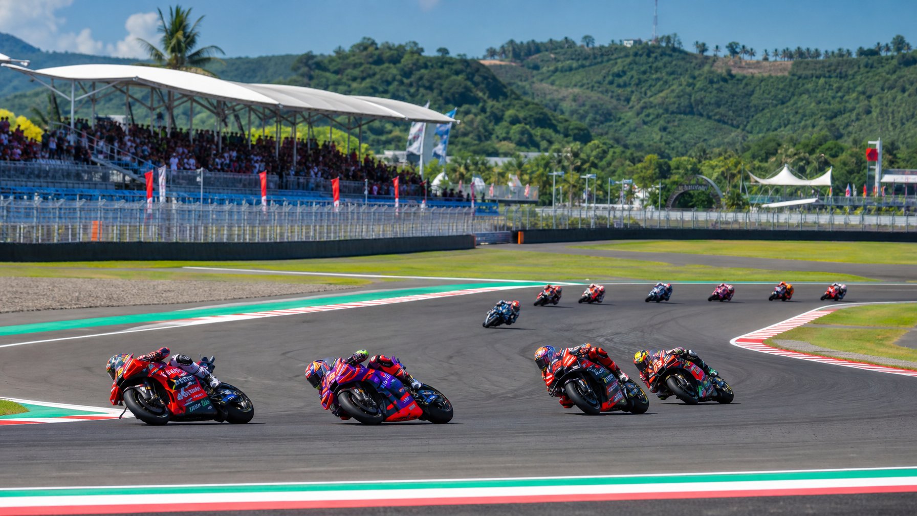 Balapan MotoGP di sirkuit Mandalika dengan motor melaju cepat dan penonton di tribun.