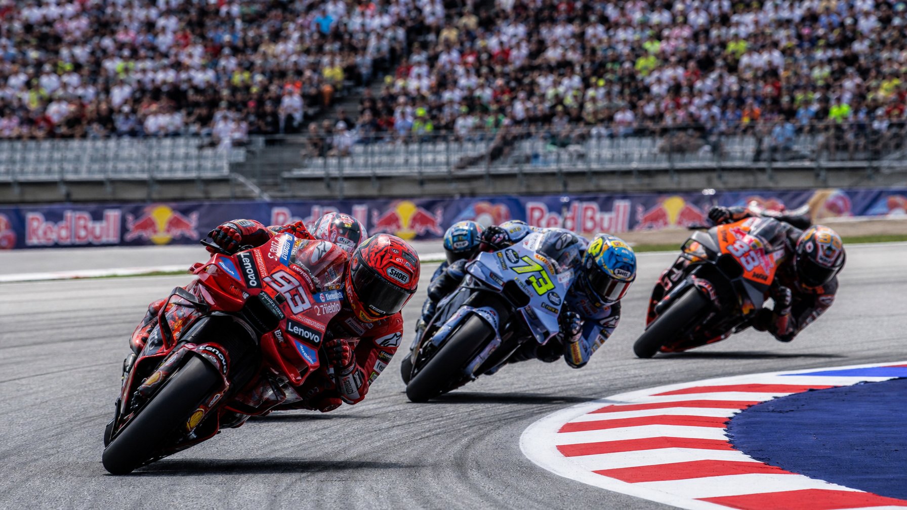 Beberapa pembalap MotoGP sedang balapan di lintasan dengan penonton di latar belakang.