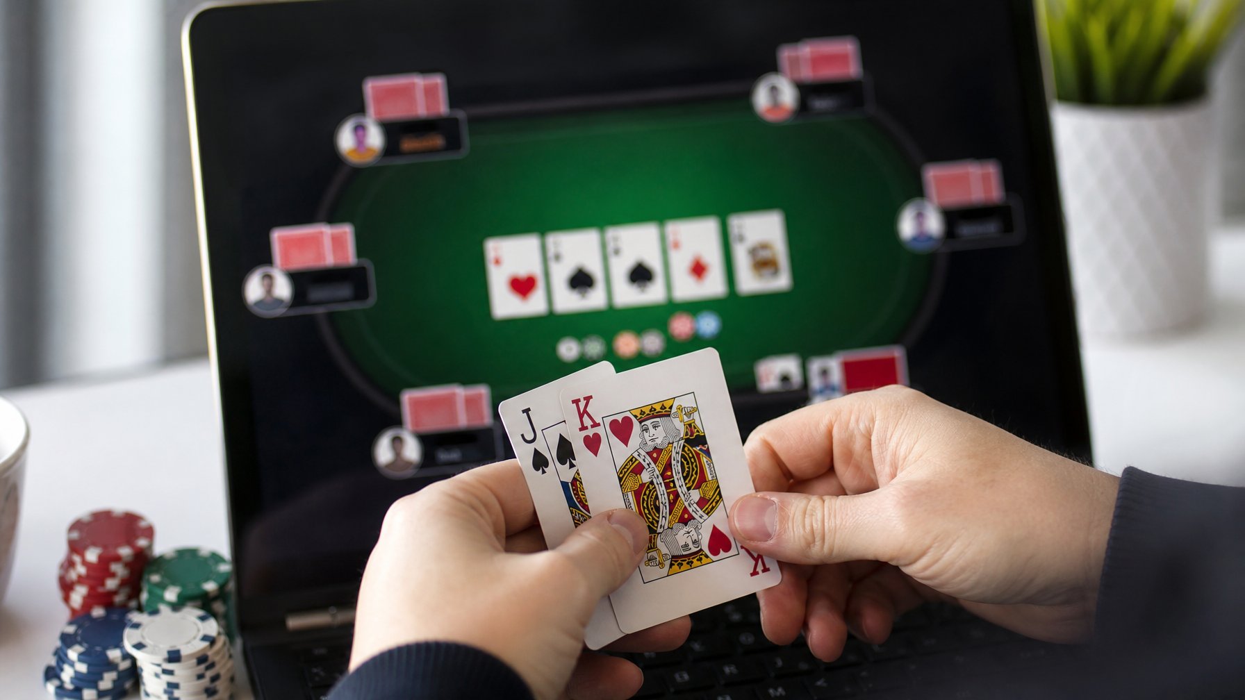 Tangan seseorang memegang kartu di meja permainan ceme online dengan chip dan kartu virtual di layar.