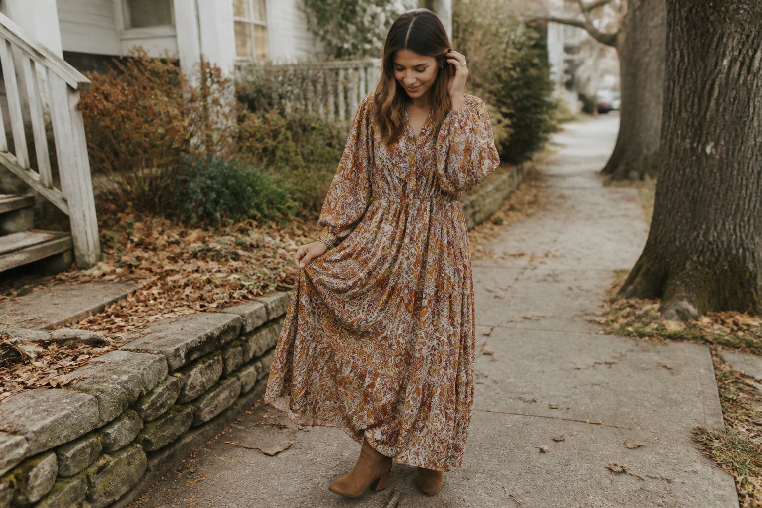 A woman in a flowing paisley maxi dress and suede ankle boots walks through an autumn outdoor setting.