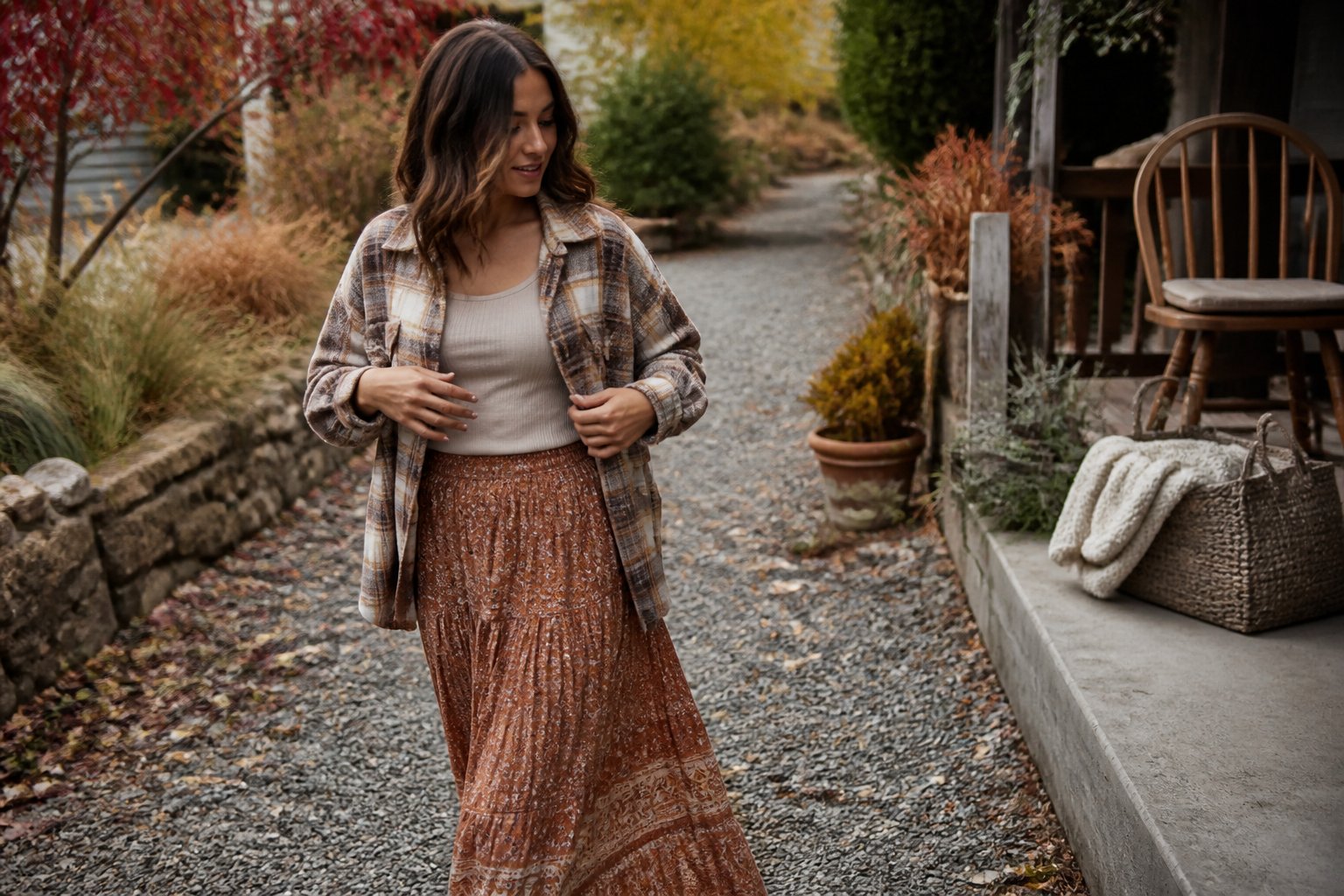 A woman wearing a plaid shacket and flowing boho skirt outdoors among autumn foliage.