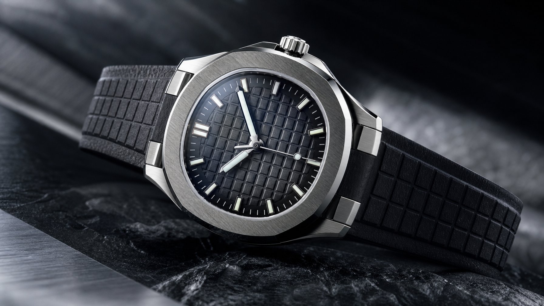 Jam tangan mewah bergaya sporty dengan tali karet gelap diletakkan di atas permukaan batu gelap.