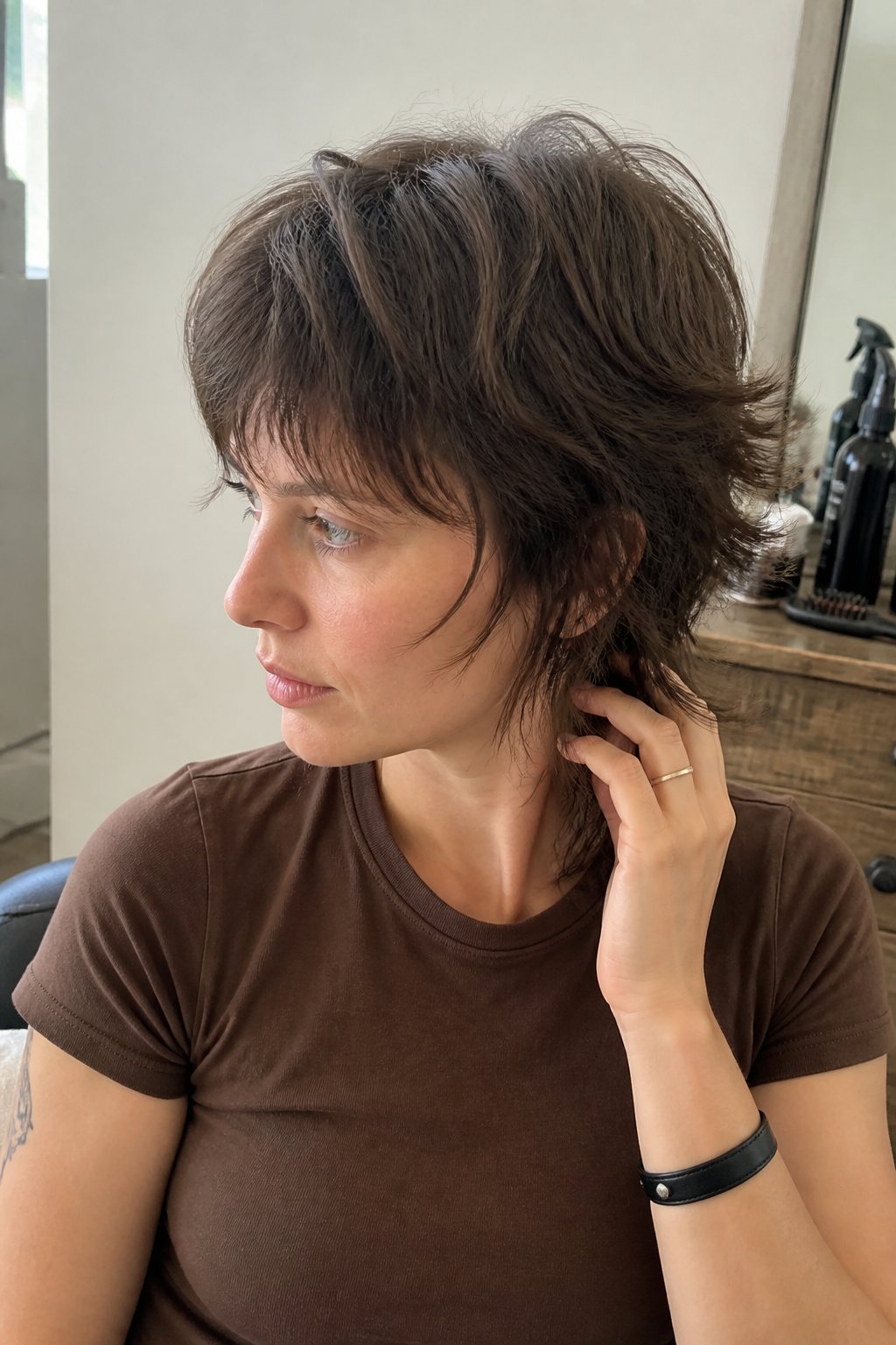 A person with a short layered wolf cut sits casually in a softly lit salon.