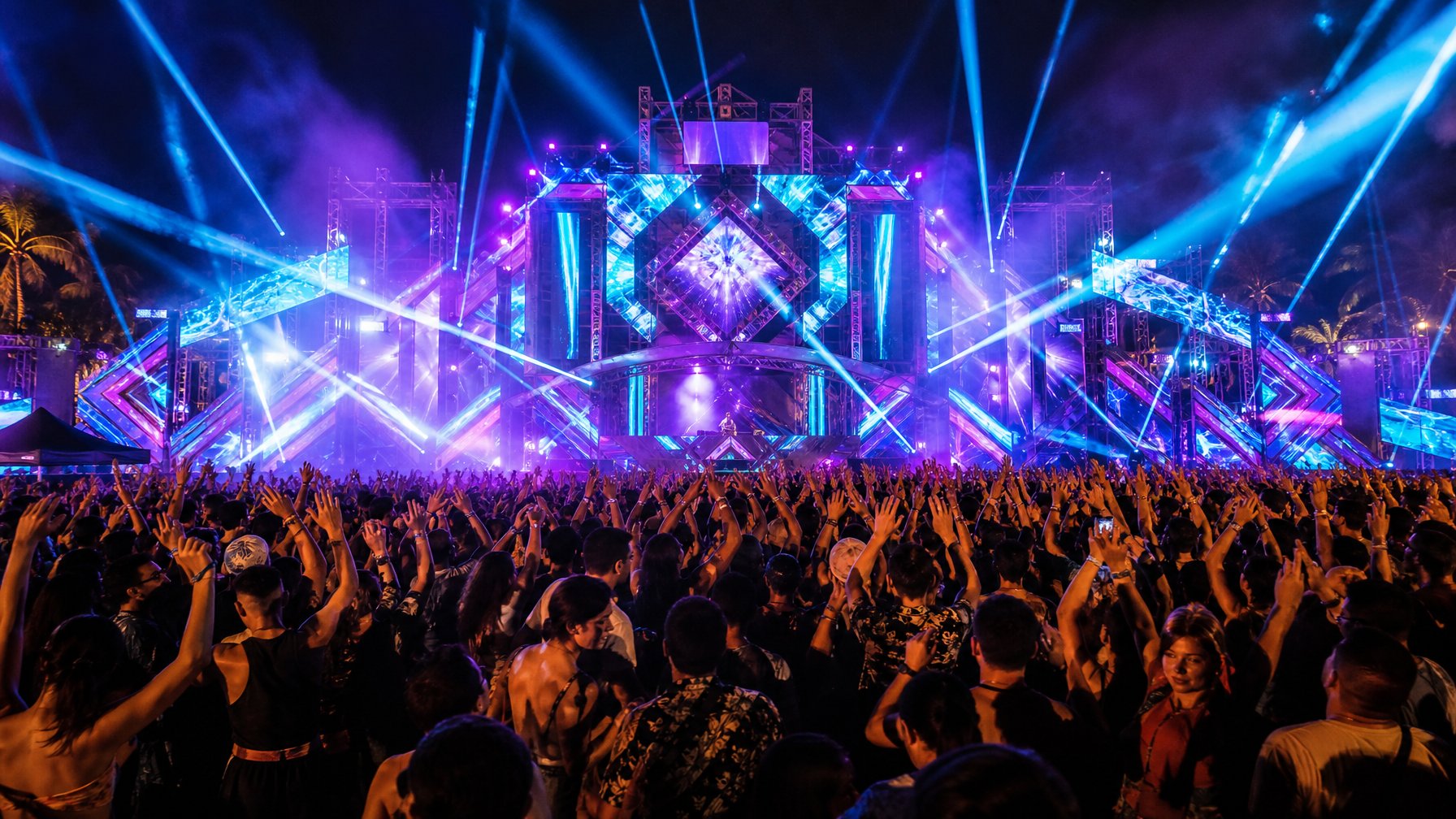 Kerumunan penonton menari di festival musik elektronik malam hari dengan panggung besar dan cahaya laser warna-warni.