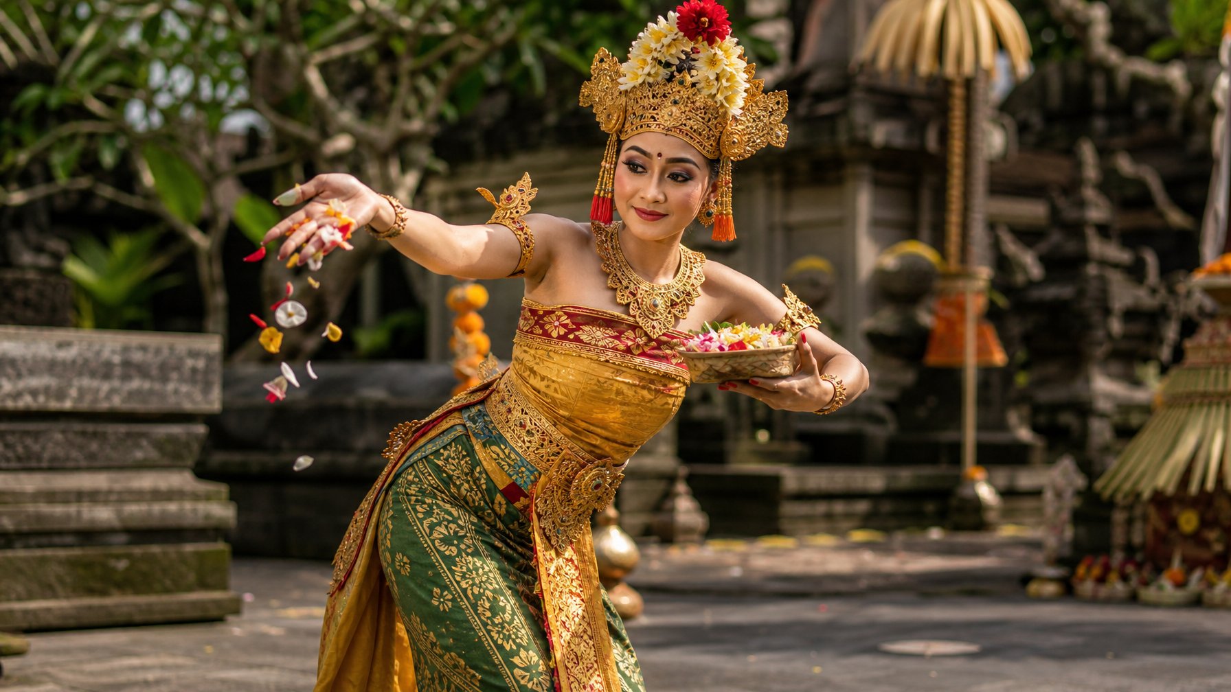 Seorang penari Bali mengenakan kostum tradisional dan menaburkan bunga dalam gerakan Tari Pendet di halaman pura.