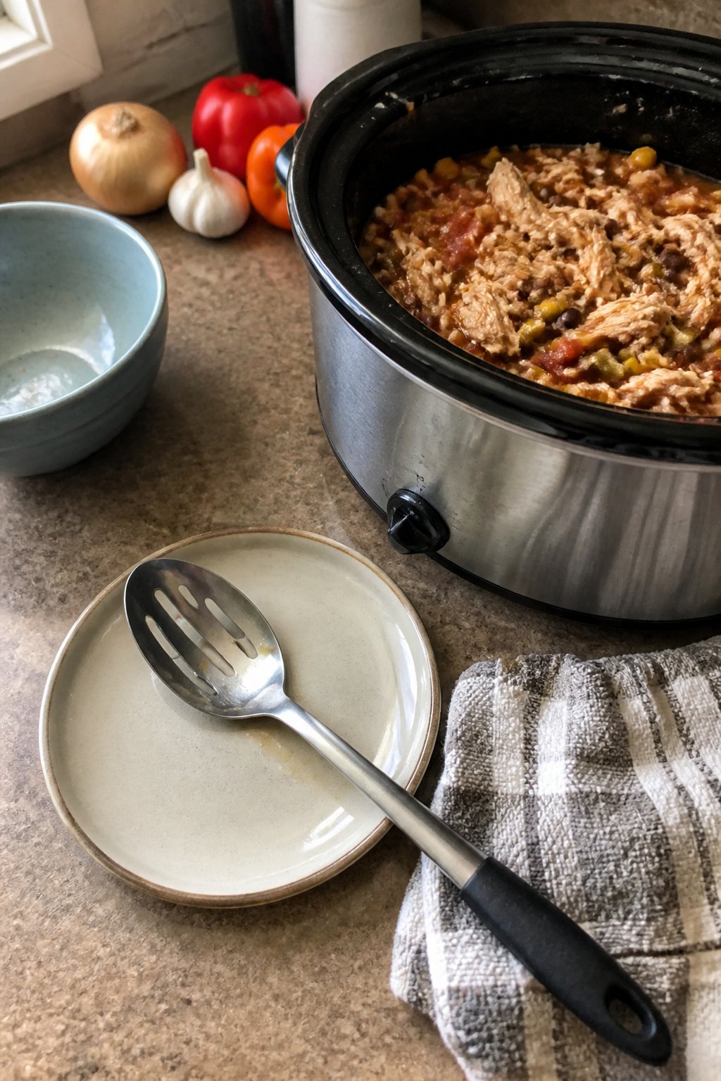 12 Crockpot Accessories That Make Dump Dinners Easier 20 A slotted spoon rests beside an open slow cooker filled with a hearty stew on a kitchen counter.