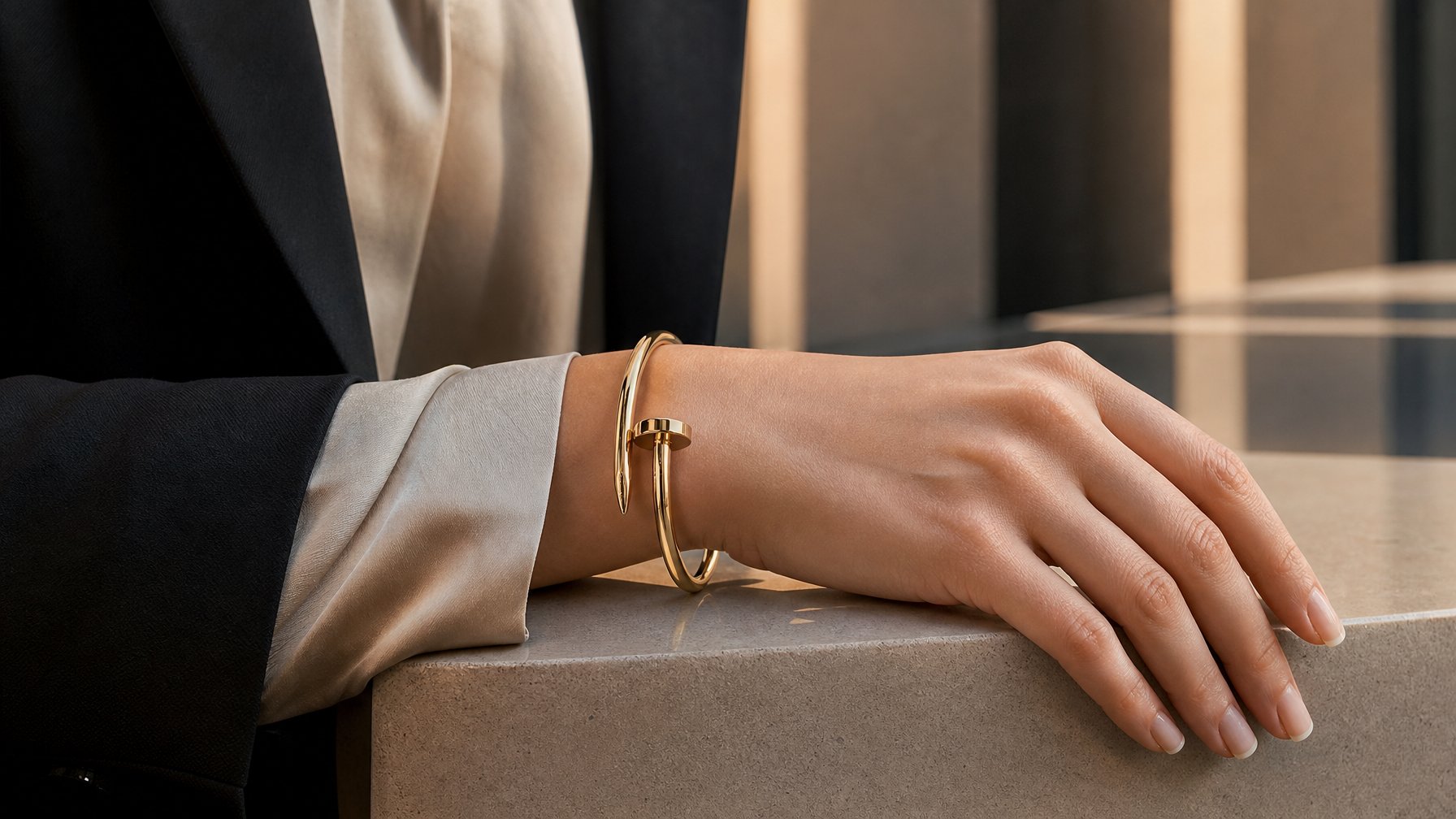 Tangan seseorang mengenakan gelang emas berbentuk paku di dalam suasana modern yang elegan.