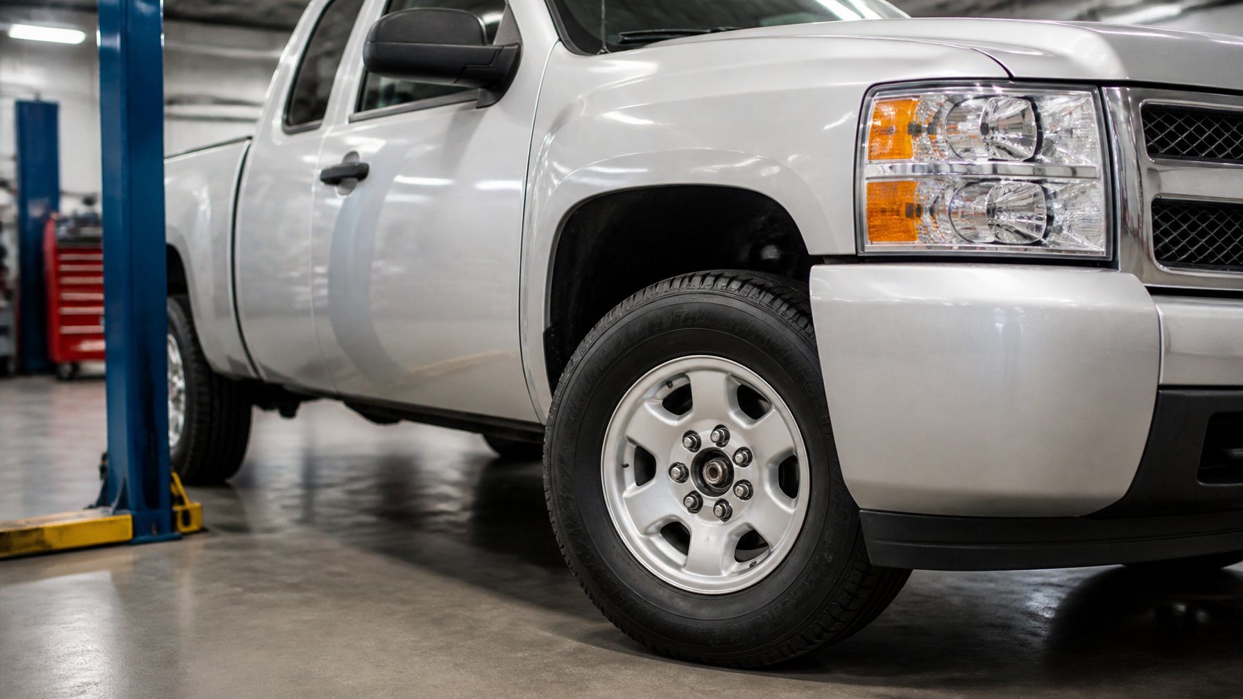 A silver Chevrolet Silverado pickup in an automotive service bay with its front wheel and five-lug hub clearly visible.