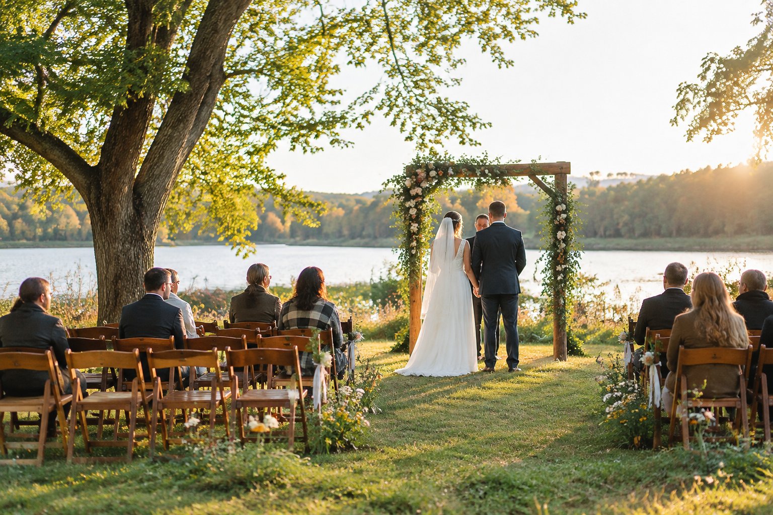 A couple exchanges vows beneath a simple floral arch in a scenic outdoor park with seated guests.