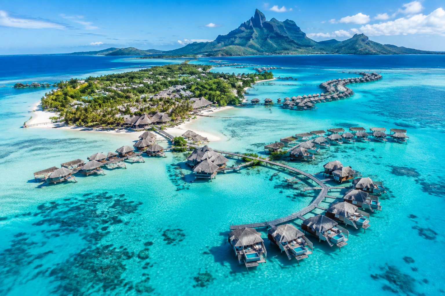 Aerial view of overwater bungalows connected by walkways around a tropical island in Bora Bora.