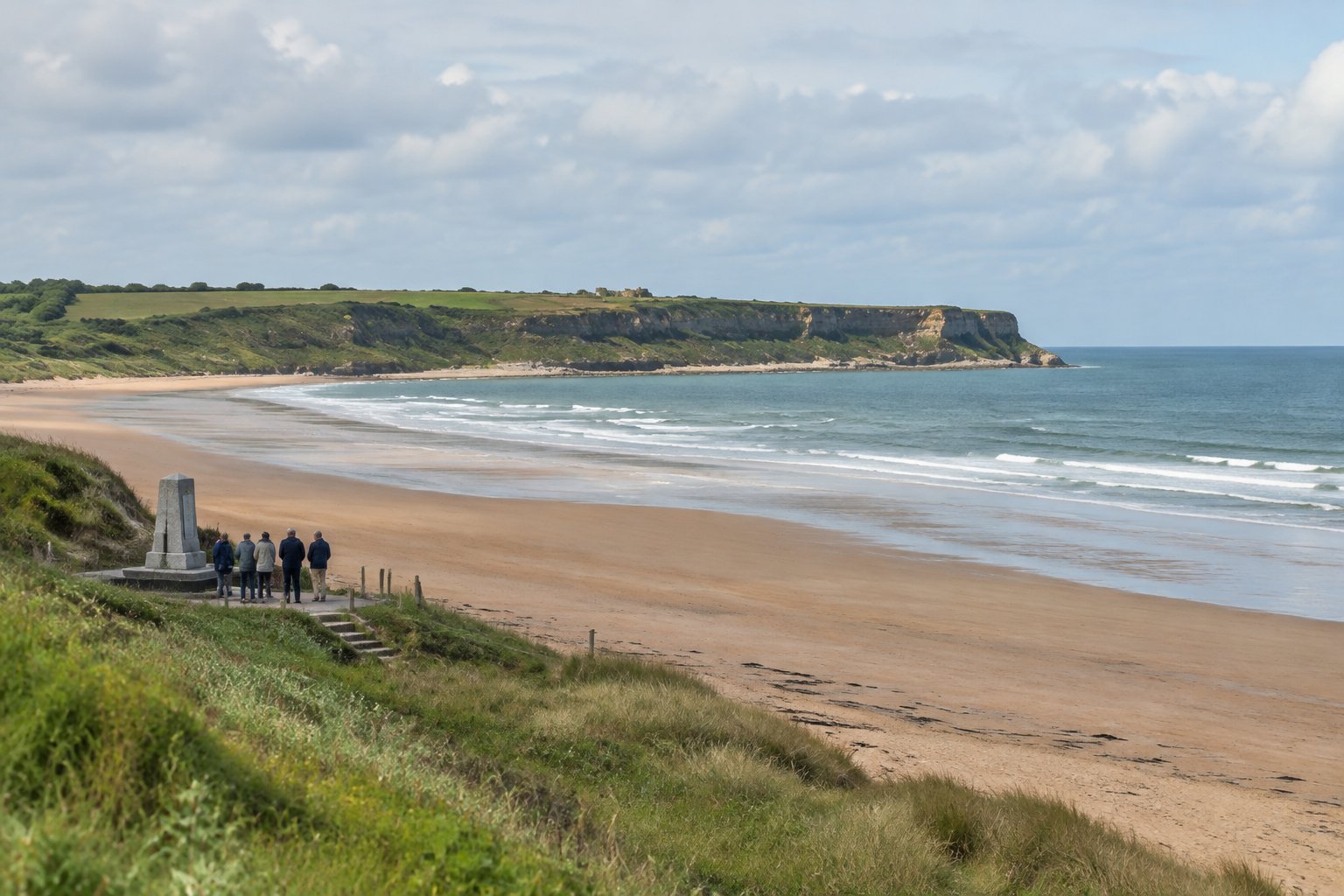 A quiet sandy Normandy beach beneath coastal cliffs, with visitors near a memorial.