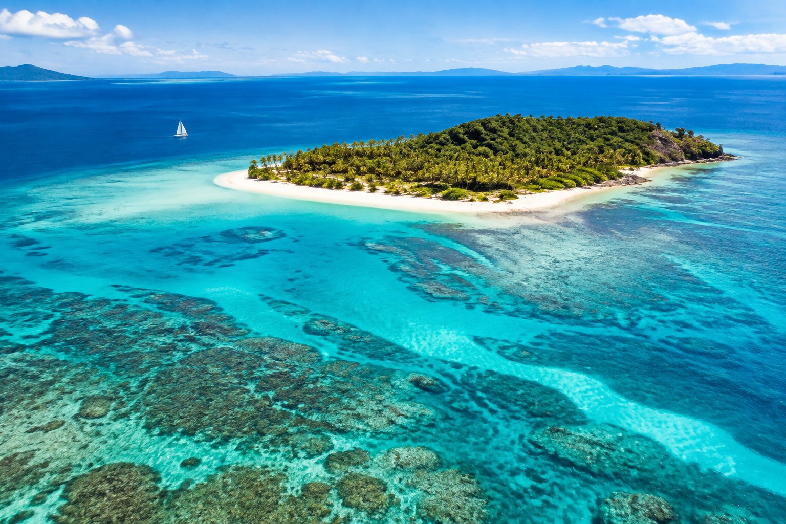 A tropical island with palm trees and white sand surrounded by turquoise water and coral reef.