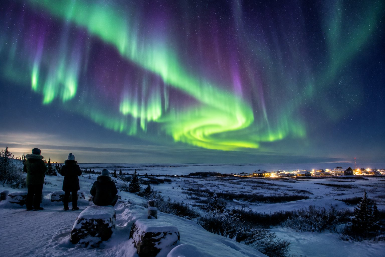 Travelers watch the northern lights over a snowy landscape near Churchill.
