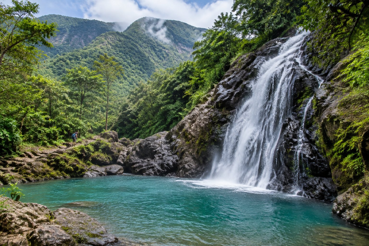 A waterfall flows into a clear pool beneath green mountains in Jarabacoa.