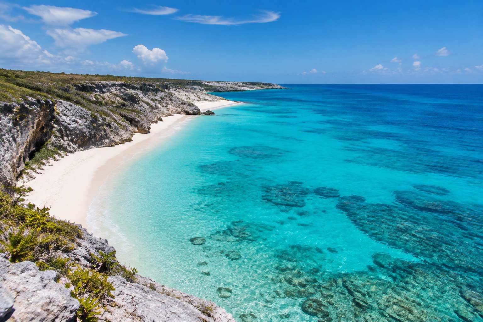 A secluded white-sand beach with clear turquoise water and rugged coastal cliffs.