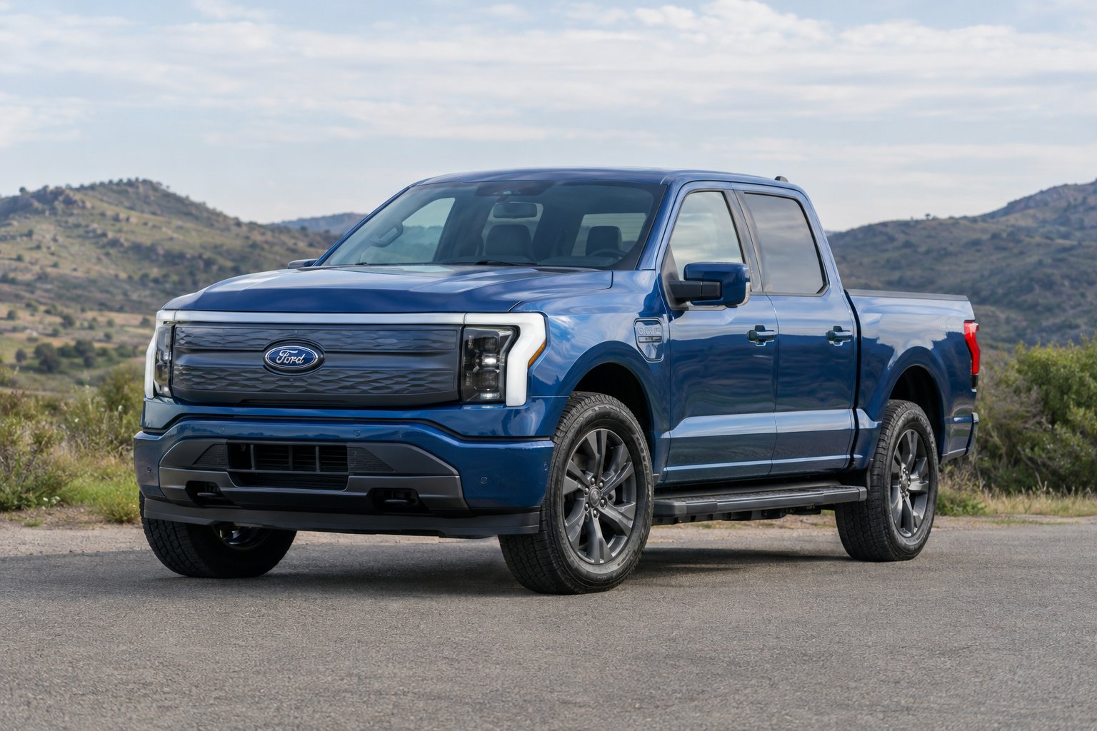An electric pickup truck parked on a paved road beside an open landscape.