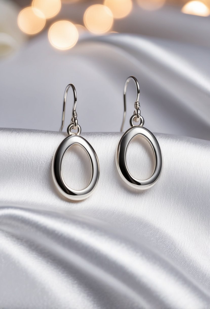 Two silver oval drop earrings on a white satin background