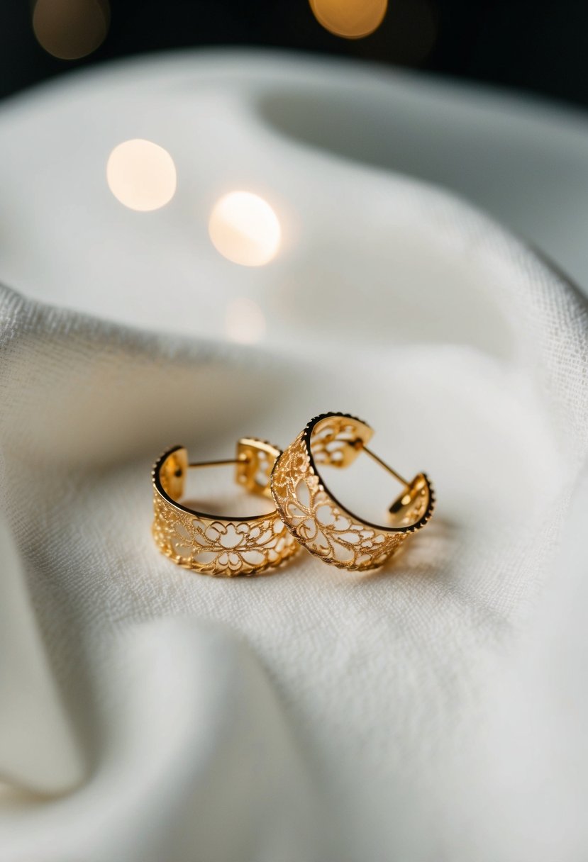 A pair of delicate lace-patterned gold earrings, resting on a soft white fabric background, with a subtle glow of light highlighting their intricate design