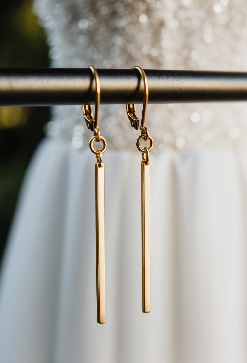 Two simple gold bars dangle from a delicate earring hook, against a backdrop of a strapless wedding dress