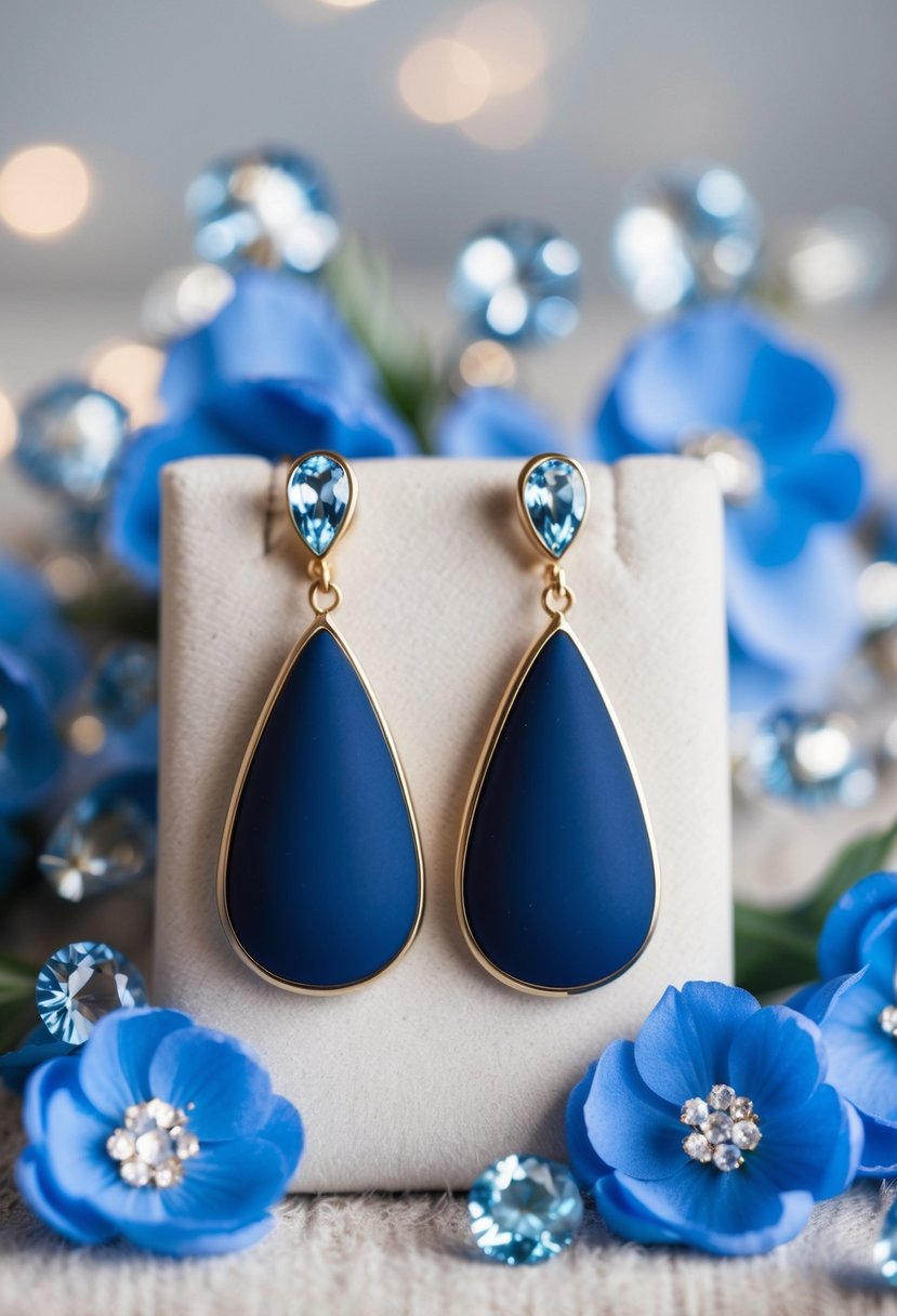 A pair of navy blue teardrop earrings displayed on a soft, velvet background, surrounded by delicate blue flowers and sparkling crystals