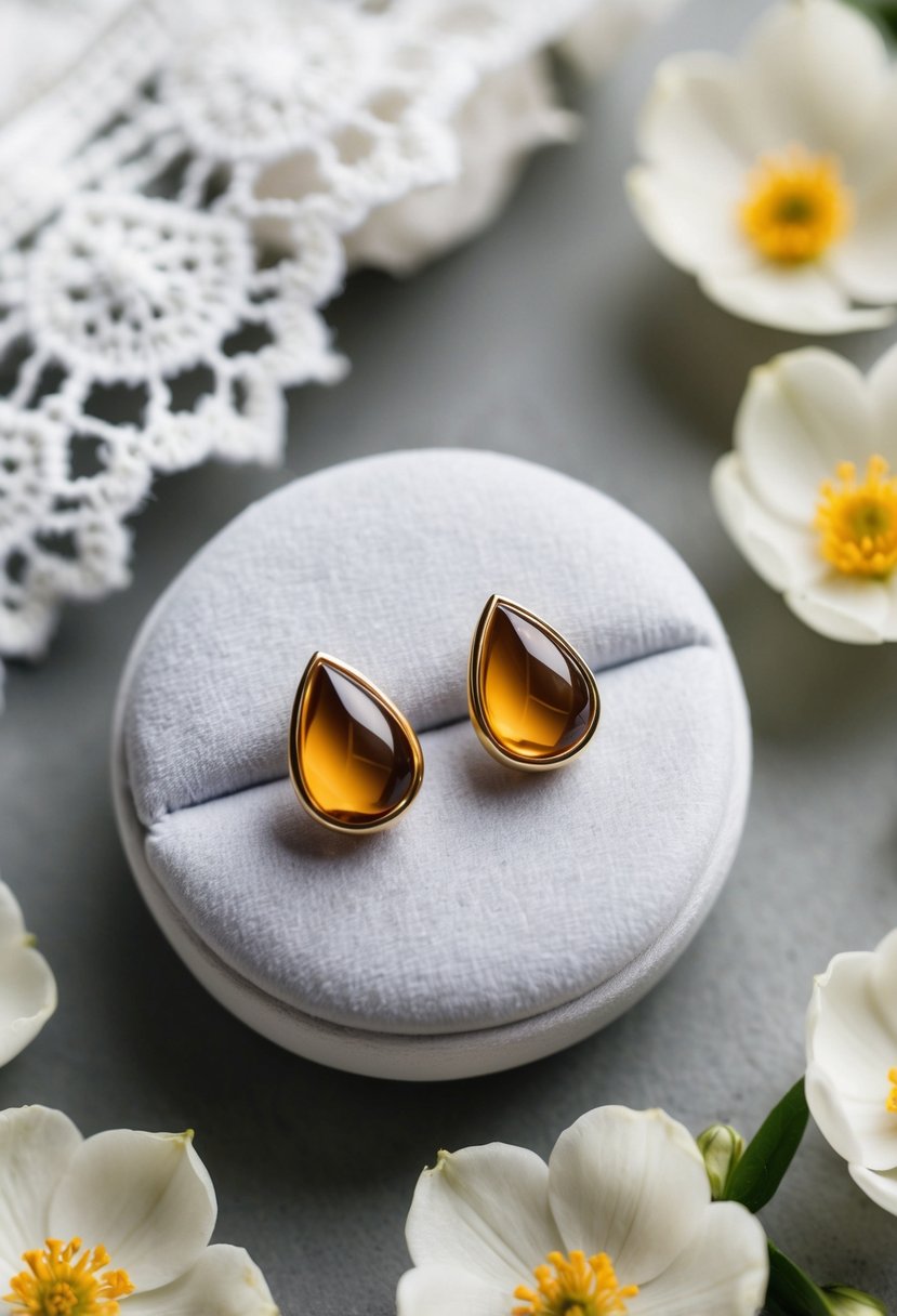 Two teardrop-shaped stud earrings on a white velvet cushion, surrounded by delicate lace and soft floral petals