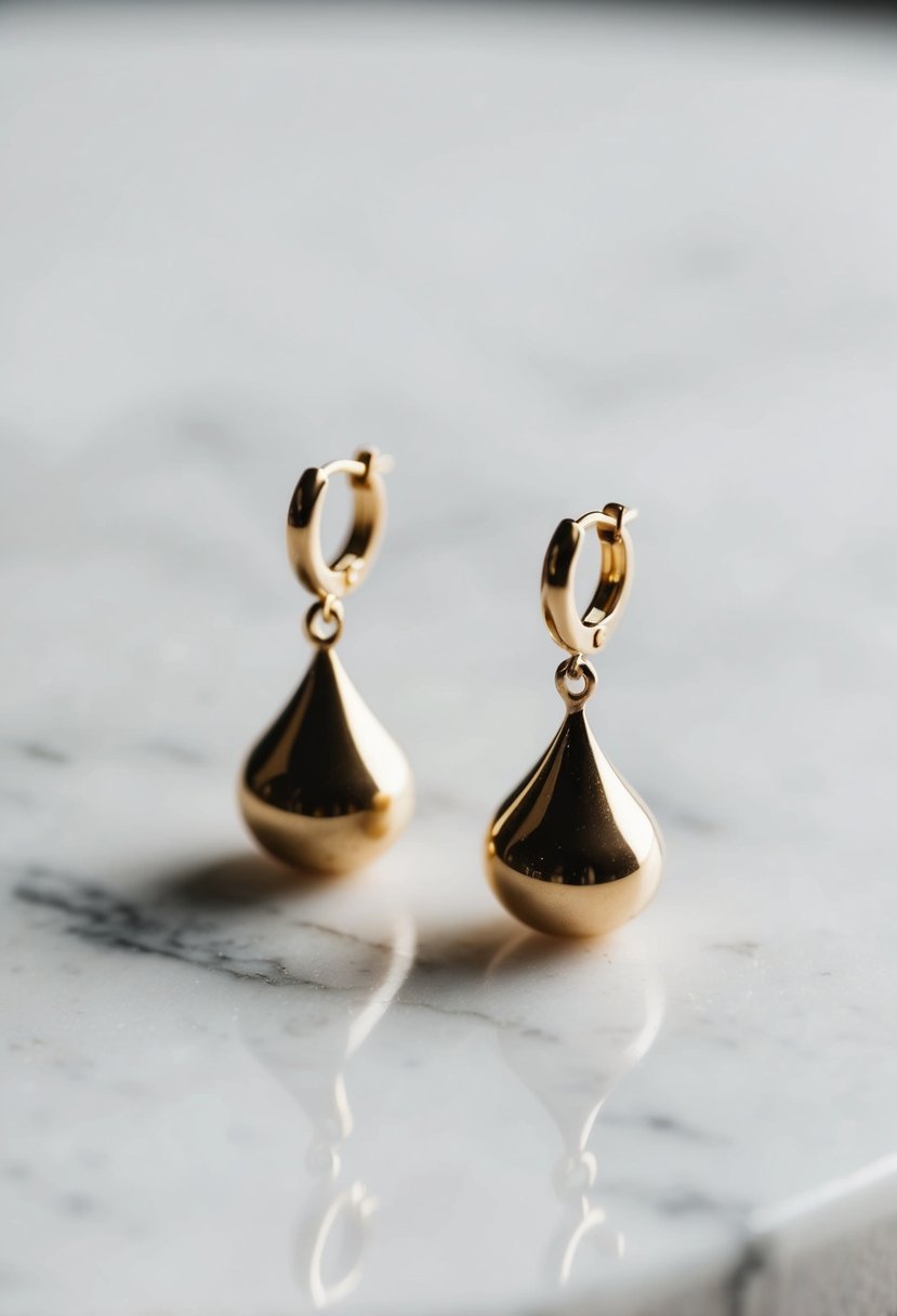 Two delicate gold drop earrings on a white marble surface