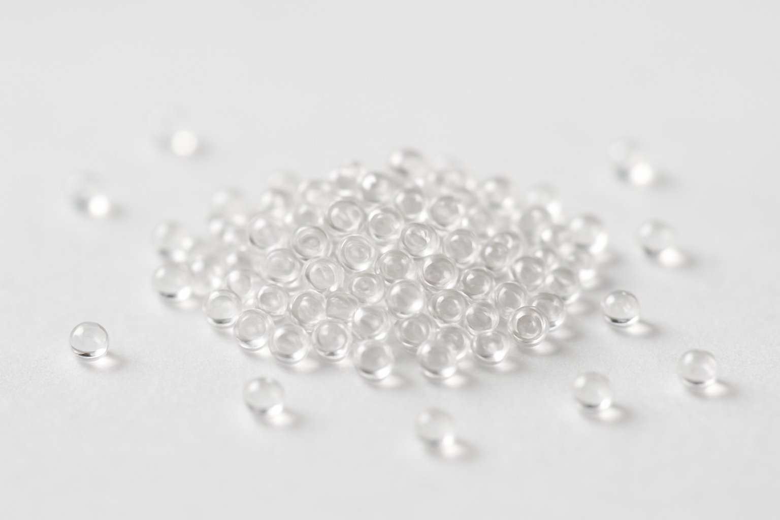 Close-up of tiny transparent glass beads scattered on a white surface.