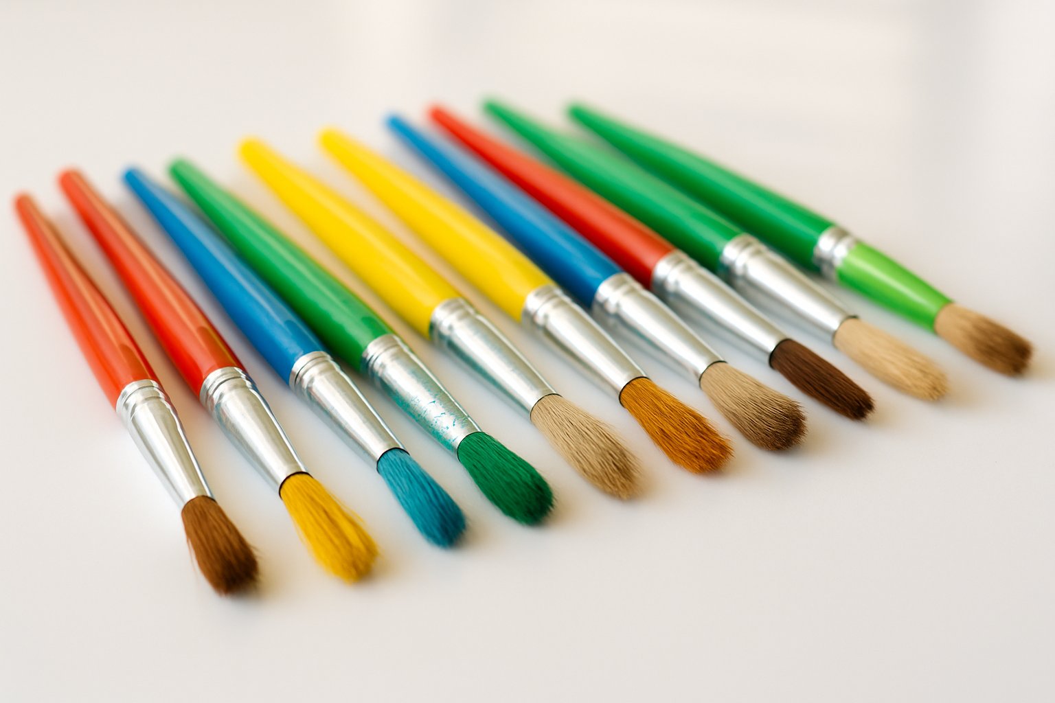 A collection of colorful kids' paintbrushes with paint on the bristles arranged on a white surface.