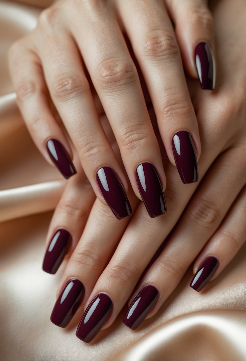Close-up of hands with deep burgundy gel polished nails resting on a soft neutral background.